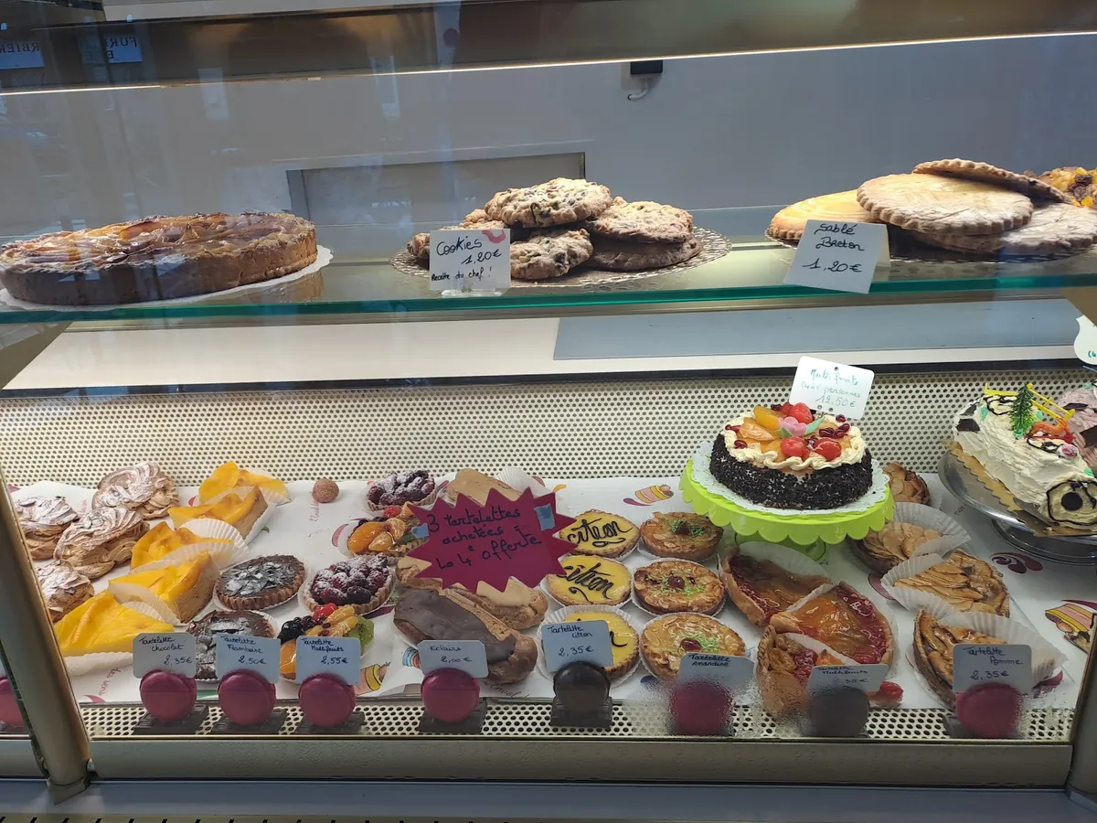 La vitrine des pâtisseries : tartes, cookies, flans, un gâteau aux fruits et des tartelettes étiquetées