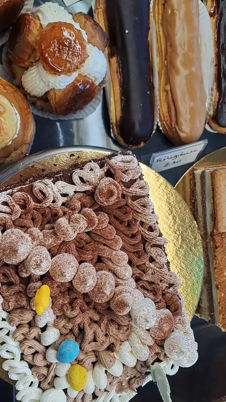 Un chou au caramel et à la chantilly, des éclairs au chocolat et au café, et un gâteau au chocolat décoré de meringues, d'œufs en sucre et d'un poussin