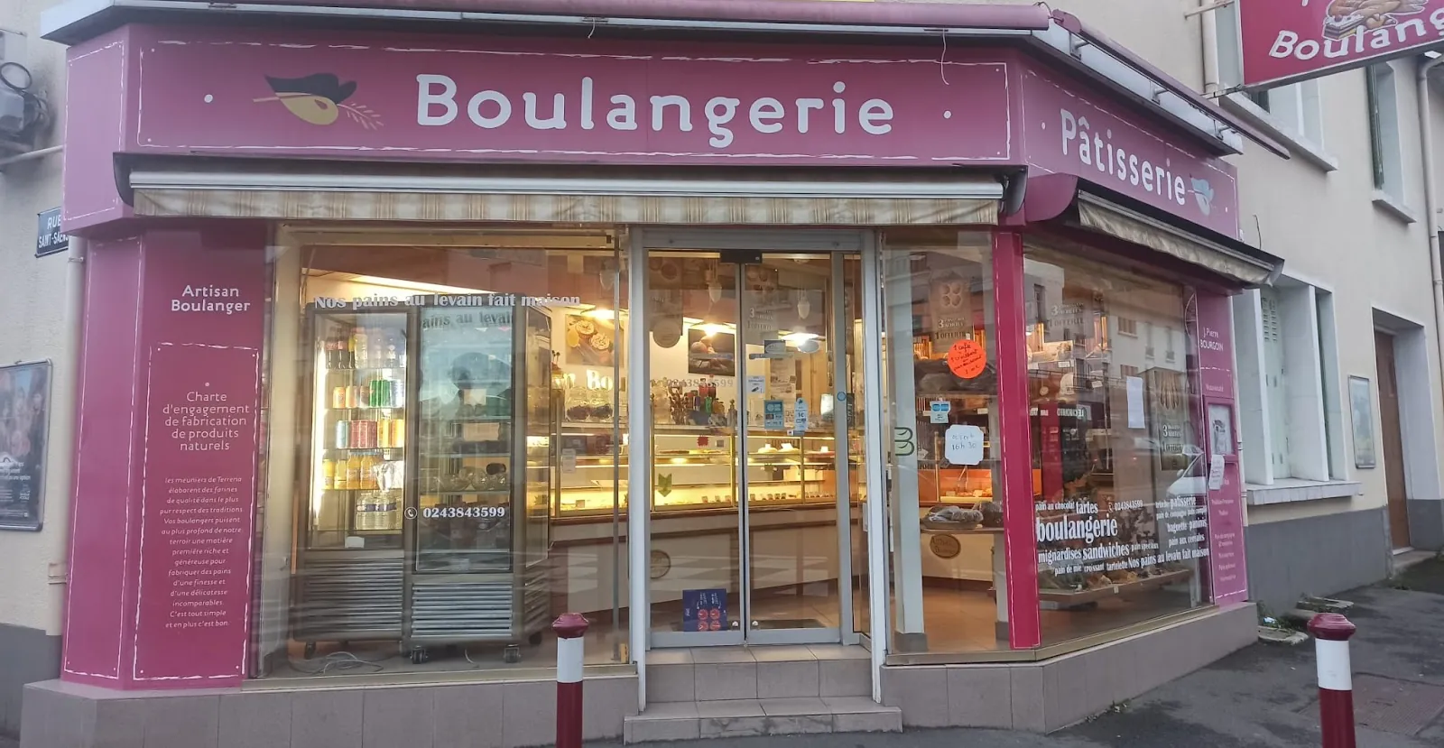 La devanture framboise de la boulangerie à l'angle de la rue, enseigne Boulangerie Pâtisserie, vitrine éclairée
