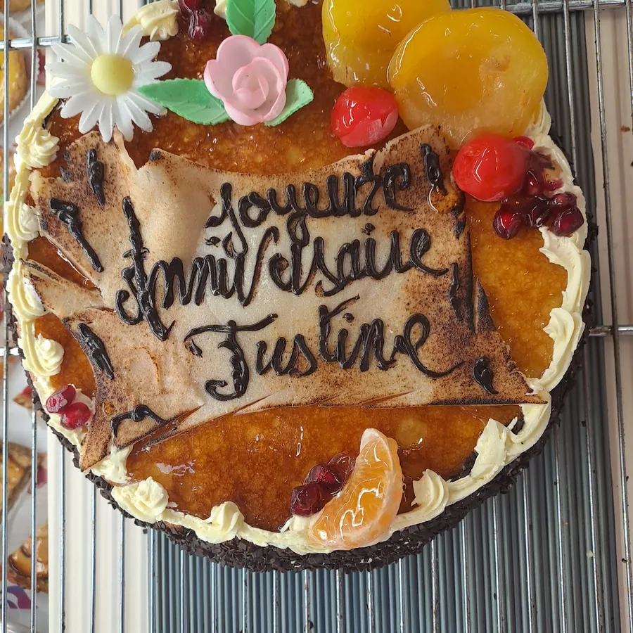 Gâteau d'anniversaire décoré de fruits confits, d'une fleur en sucre et d'un message écrit au chocolat
