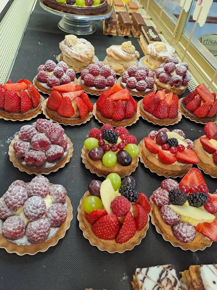 Tartelettes aux framboises, aux fraises et aux fruits rouges alignées dans la vitrine, des choux à la crème au fond